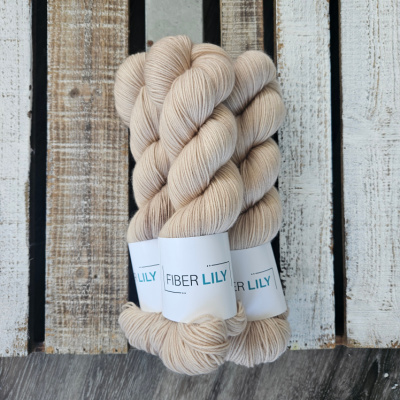 Three skeins of tonal taupe neutral coloured hand dyed yarn in a pile on a wooden background