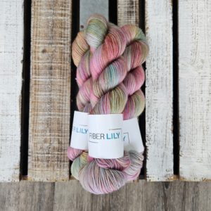Three skeins of pink, blue and olive coloured hand dyed yarn on a wooden background