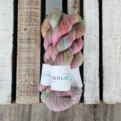 Three skeins of pink, blue and olive coloured hand dyed yarn on a wooden background