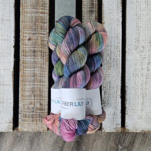 Three skeins of pink and purple coloured hand dyed yarn next to their knit and crochet swatches