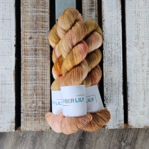 Three skeins of warm neutral coloured hand dyed yarn next to their knit and crochet swatches