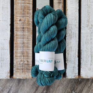 Three skeins of tonal forest green coloured hand dyed sock yarn in a pile on a wooden background