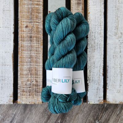 Three skeins of tonal forest green coloured hand dyed sock yarn in a pile on a wooden background