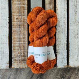 Three skeins of tonal orange coloured hand dyed sock yarn in a pile on a wooden background