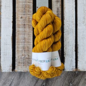 Three skeins of tonal yellow coloured hand dyed sock yarn in a pile on a wooden background