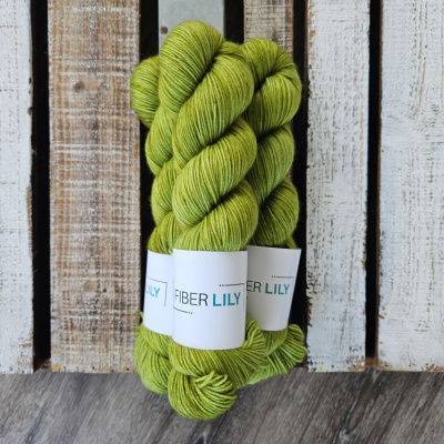 Three skeins of tonal green coloured hand dyed sock yarn in a pile on a wooden background