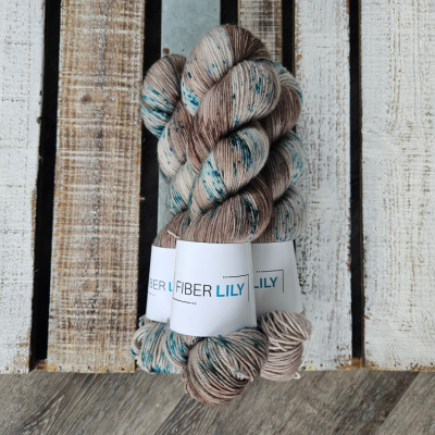 Three skeins of brown yarn with teal speckles in a pile on a wooden board