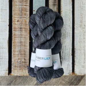 A pile of three skeins of yarn dyed gun metal grey laying on a wood backdrop