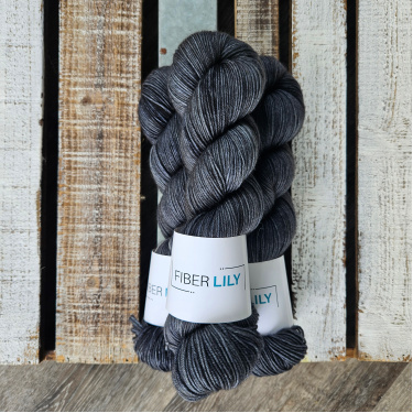A pile of three skeins of yarn dyed gun metal grey laying on a wood backdrop