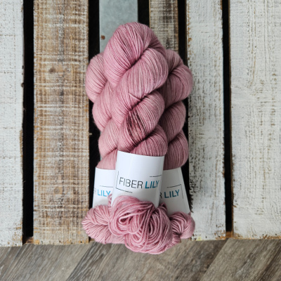 A pile of three hanks of hand dyed yarn dyed a muted pink colour
