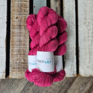 Three skeins of deep fuchsia pink hand dyed yarn on a wooden board