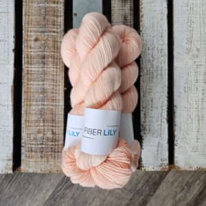 Three skeins of delicate apricot coloured hand dyed yarn on a wooden board