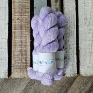 Three skeins of lilac purple hand dyed yarn on a wooden board
