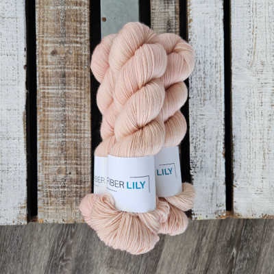 Three skeins of tonal blush pink coloured hand dyed sock yarn in a pile on a wooden background