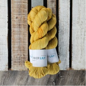 Three skeins of tonal sand coloured hand dyed sock yarn in a pile on a wooden background