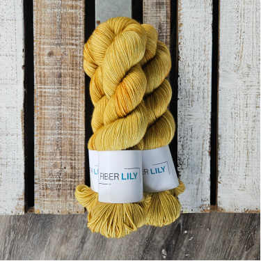 Three skeins of tonal sand coloured hand dyed sock yarn in a pile on a wooden background