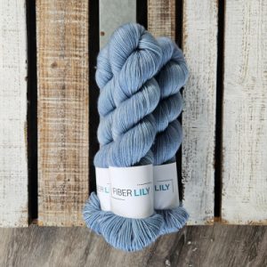 Three skeins of tonal baby boy blue coloured hand dyed sock yarn in a pile on a wooden background