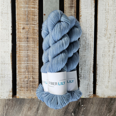 Three skeins of tonal baby boy blue coloured hand dyed sock yarn in a pile on a wooden background