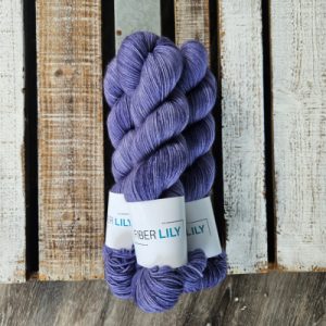 Three skeins of tonal periwinkle coloured hand dyed sock yarn in a pile on a wooden background