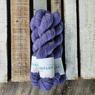 Three skeins of tonal periwinkle coloured hand dyed sock yarn in a pile on a wooden background