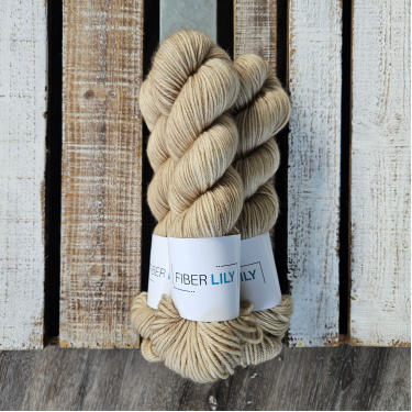 Three skeins of tonal green leaning taupe coloured hand dyed yarn in a pile on a wooden background
