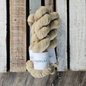 Three skeins of tonal green leaning taupe coloured hand dyed sock yarn in a pile on a wooden background