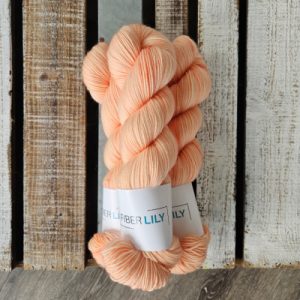 Three skeins of tonal apricot coloured hand dyed sock yarn in a pile on a wooden background