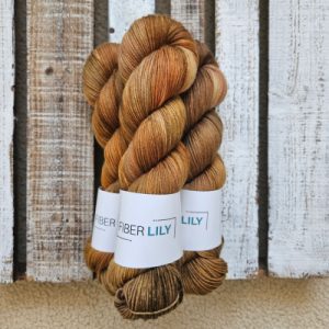 Three skeins of variegated golds and earth tone hand dyed sock yarn representing Spring colours on a wooden background