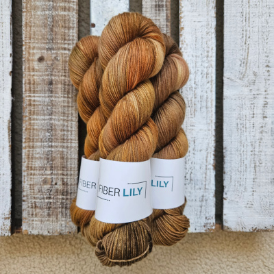Three skeins of variegated golds and earth tone hand dyed sock yarn representing Spring colours on a wooden background