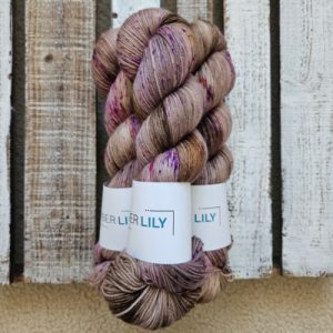 Three skeins of hand dyed pecan brown sock yarn speckled raspberry, violet and citrus representing Spring colours on a wooden background