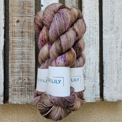 Three skeins of hand dyed pecan brown sock yarn speckled raspberry, violet and citrus representing Spring colours on a wooden background