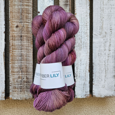 Three skeins of variegated purple, chestnut hand dyed sock yarn representing Spring colours on a wooden background
