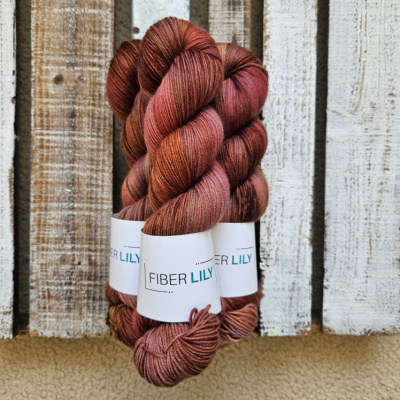Three skeins of variegated purple, crimson, gold and pecan hand dyed sock yarn representing Spring colours on a wooden background
