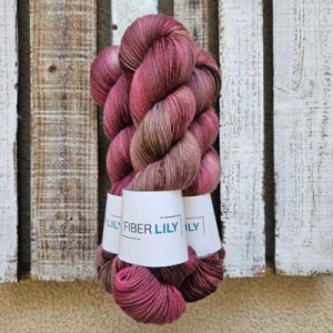 Three skeins of variegated muted crimson and pecan hand dyed sock yarn representing Spring colours on a wooden background