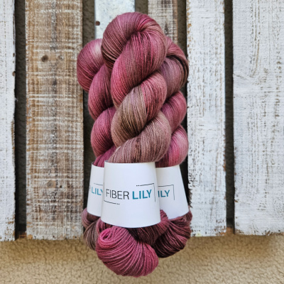 Three skeins of variegated muted crimson and pecan hand dyed sock yarn representing Spring colours on a wooden background