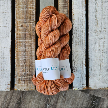 Three skeins of warm tonal caramel hand dyed DK yarn on a wooden background