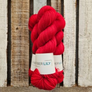 Three skeins of clear red tonal hand dyed sock yarn on a wooden background