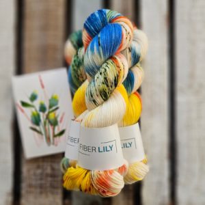 Three skeins of blue, yellow, orange and cream hand dyed sock yarn representing an original watercolour painting on a wooden background