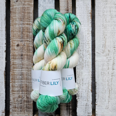 Skeins of aqua green, forest greens, gold and lilac hand dyed sock yarn on a wooden background