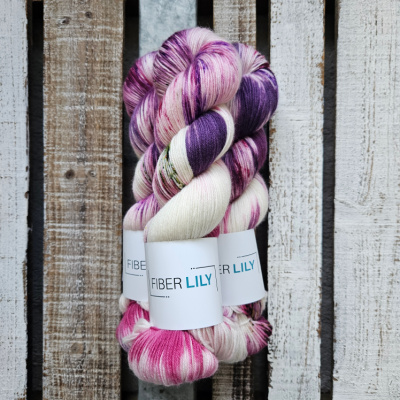 Skeins of pink, purple, green and violet hand dyed sock yarn on a wooden background