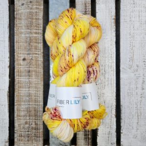 Skeins of gold and raspberry speckled hand dyed DK yarn on a wooden background
