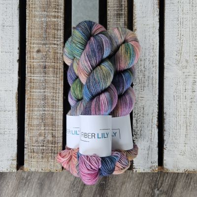 Three skeins of pink and purple coloured hand dyed yarn next to their knit and crochet swatches