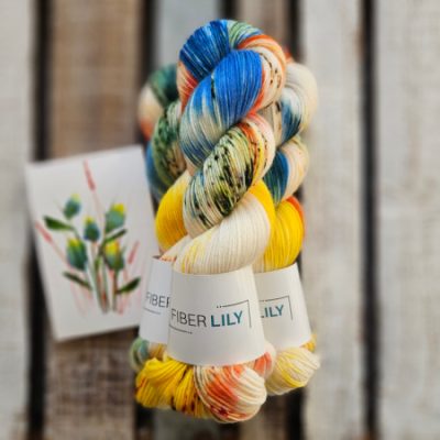 Three skeins of blue, yellow, orange and cream hand dyed sock yarn representing an original watercolour painting on a wooden background