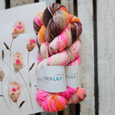 Three skeins of pink, brown, orange and cream hand dyed sock yarn representing an original watercolour painting on a wooden background
