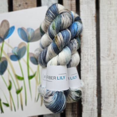 Skeins of blue, brown, green and cream hand dyed sock yarn representing an original watercolour painting on a wooden background